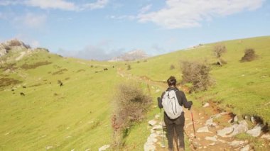 Bir kadın Gorbea Doğal Parkı 'nın geniş ve açık arazisini keşfederek yürüyüş direkleri ve sırt çantasıyla donatılmıştır. Sahne, doğanın sükunetini ve güzelliğini yakalar.