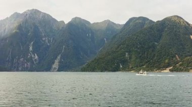 Yeni Zelanda 'daki Milford Sound' un nefes kesici manzarası, görkemli dağların dingin sularla buluşmasını gösteriyor, küçük bir tekne ölçek ve sükunet hissi ekliyor.