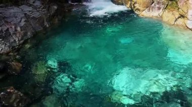 Yeni Zelanda, Milford Sound 'da şelalenin sakin manzarası, yemyeşil ve engebeli uçurumlarla çevrili. Kristal berrak su doğanın sükunetini yansıtır.