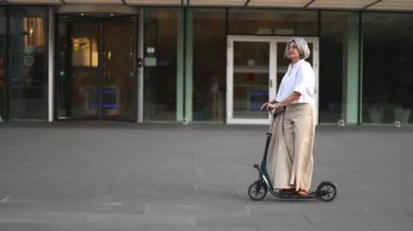 Olgun bir iş kadını, şehir içi seyahatine modern bir yaklaşım sergileyerek, mobiletiyle şehir sokaklarında dolaşıyor. Profesyonel bir ortamda özgüven ve zarafet gösteriyor..