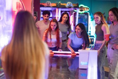 Bir grup arkadaş neşeli bir hokey oyununun keyfini çıkarıyorlar, neşe dolu, eğlenceli bir oyun salonunda, kahkaha ve heyecanla dolu.