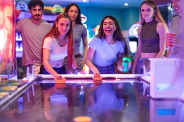 Renkli bir oyun salonunda hokey oynayan bir grup genç arkadaş birlikte boş zamanlarının tadını çıkarıyorlar.