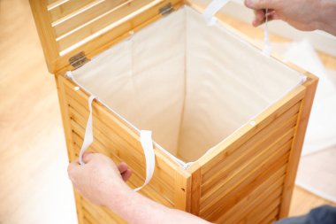 Eller yeni ahşap bambu çamaşır sepetinin içine beyaz bez döşüyordu.