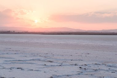 Larnaca tuz gölü havaalanının yanında, arka planda dağlar, gün batımında yel değirmenleri ve kıpkırmızı gökyüzü, Kıbrıs
