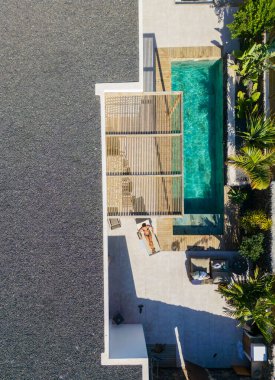 Lüks bir tatil köyünde, özel bir yüzme havuzunun yanında güneşlenen bir kadının hava manzarası.
