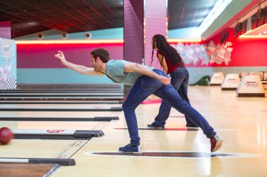 Bowling salonunda bowling topu atan genç bir adam ve arka planda onu izleyen bir kadın.