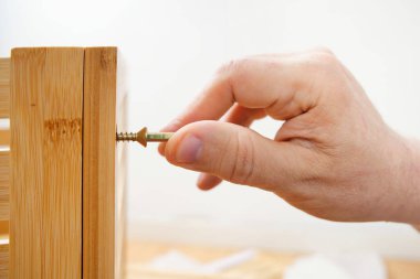 Bir marangozun eli montaj sırasında ahşap bir mobilyaya vida sıkıyor.