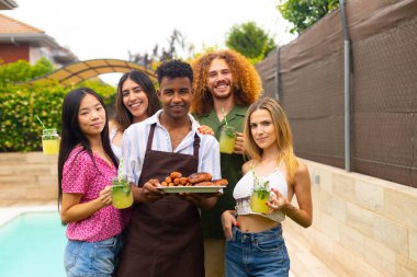 Neşeli çeşitli arkadaşlar barbekü yapıyorlar, ızgara yemek ve limonata tutuyorlar, yaz partisinde havuz başında eğleniyorlar.