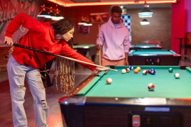 İki genç yetişkin, renkli, neon ışıklı bilardo odasında bilardo oynuyorlar, dostça bir oyun oynuyorlar.