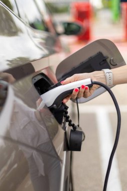 Elektrikli araba şarjına takılı güç kablosu yerleştiren kadının elini kapat, yeşil enerji kavramı