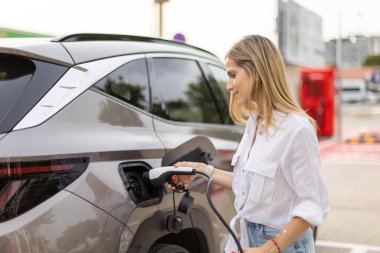 Genç iş kadını, halka açık bir şarj istasyonunda elektrikli arabasını şarj ediyor, sürdürülebilir ulaşım ve çevre dostu uygulamaları teşvik ediyor