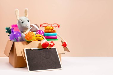 Kutu içinde çocuklar için oyuncaklar. Tahtada yazılı boş yazı var. Bej arka planda, az sayıda yaşam tarzı var. Oyuncak bağış kavramı, çocuklar için hayır kurumu.