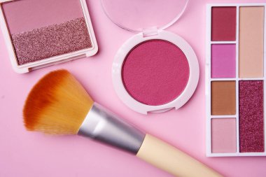 Pembe ve kırmızı makyaj ürünlerinin çeşitli tonlarında allık, göz farı ve fırça pembe bir yüzeye yerleştirilir.