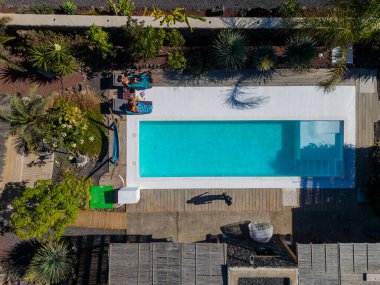 Dikdörtgen yüzme havuzlu, turistlerin güneşlendiği, sakin ve davetkar bir tatil deneyimi sunan lüks bir tatil beldesinin havadan görünüşü.