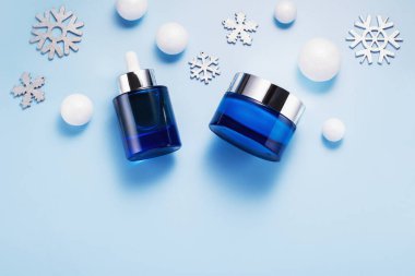 Mavi arka planda kozmetik ürünleri ve tatil temalı dekorasyonlarla kış cilt bakımı konsepti, üst görünüm, kopyalama alanı