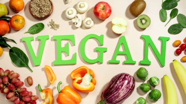Taze meyve, sebze ve bir kase mercimek ve vejetaryen diyeti ile çevrili bej masanın üzerinde büyük yeşil harflerle VEGAN kelimesi