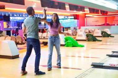 İki arkadaş başarılı bir bowling maçını kutluyor, beşlik çakıyor ve aydınlık bir sokağın canlı atmosferinin tadını çıkarıyor.