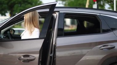 Sarışın kadın araca biniyor, oturuyor, emniyet kemerini takarak emniyet kemerini takıyor, yol güvenliğini gösteriyor.