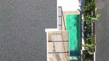 Minimalist, turkuaz yüzme havuzlu, ahşap güverteli, çakıl bahçeli ve palmiye ağaçlı bir villa.