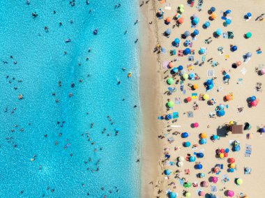 Kumlu sahildeki renkli şemsiyeler, güneşli yaz günlerinde mavi denizde yüzen insanlar. Mallorca, Balear Adaları, İspanya. Berrak gök mavisi suyu olan tropik bir yer. Seyahat et. Üst görünüm