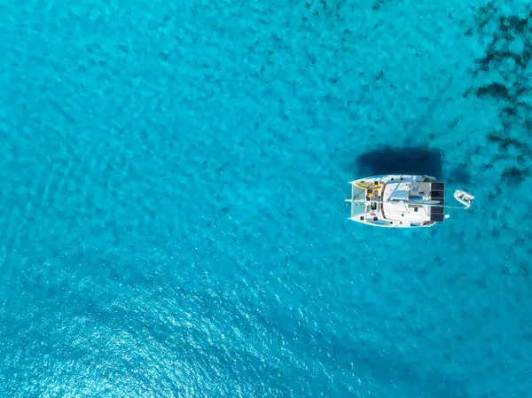 İspanya 'nın Balear Adaları, Mallorca açıklarındaki kristal berrak turkuaz sularda demirli bir yatın havadan görünüşü. Katamaran ve mavi denizin üst drone görüntüsü. Tropik bir manzara. Seyahat