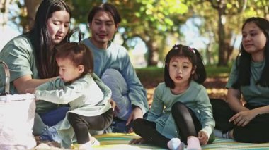 Asyalı aile, Yeni Zelanda 'da renkli sonbahar yaprakları arasında rahatlatıcı bir pikniğin tadını çıkarıyor. Sıcak ve güneşli bir gün mevsimin güzelliğini vurguluyor, hatıralar yaratıyor.