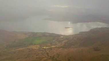 Wanaka Gölü 'nün sonbaharda nefes kesici hava manzarası. Güneş ışığı bulutları nazikçe delip geçer, aşağıdaki yemyeşil, renkli manzaranın üzerine huzur verici bir ışık saçar..