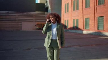 Profesyonel bir trans kadın telefonda konuşurken, dışarıda çalışırken güvenle yürür. İş ortamında bir klasör, güçlendirme ve çeşitlilik taşıyor.