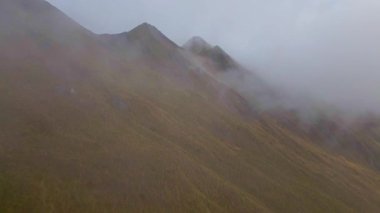 Wanaka, Yeni Zelanda 'daki Roys Tepesi' ndeki puslu sonbahar tepeleri, turuncu ve kahverengi zengin renkleri, kayan bulutlar ve dramatik bir gökyüzü ile kaplanmış huzurlu bir manzara sergiliyor..