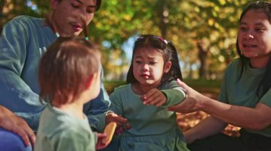 Asyalı bir aile Yeni Zelanda 'da renkli sonbahar yapraklarıyla çevrili neşeli bir piknik yapıyor. Ebeveynler ve çocuklar kahkaha ve atıştırmalıkları paylaşıyor, mevsimin güzelliğini kucaklıyorlar.