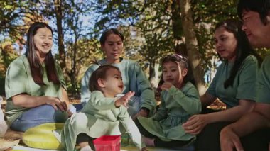 Asyalı bir aile sonbahar pikniği için Yeni Zelanda parkında renkli bir battaniyede toplanıyor. Atıştırmalıkları, kahkahaları ve sonbaharın güzelliğini, canlı yapraklarla çevrili olarak severler.