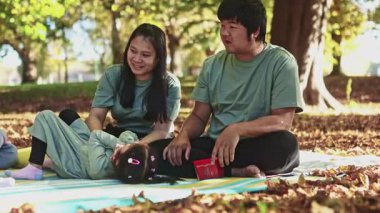 Asyalı bir aile, Yeni Zelanda 'nın canlı sonbahar manzarasının ortasında, renkli yapraklarla çevrili ve açık mavi gökyüzünün altında rahatlatıcı bir pikniğin tadını çıkarıyor.