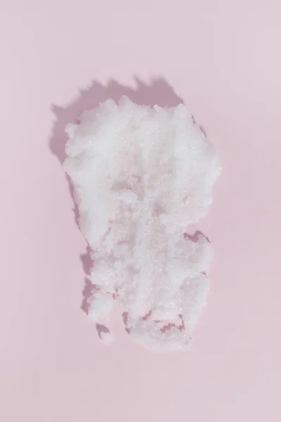 White sugar scrub smear smudge swatch on pink background. Natural cosmetic skin exfoliation product sample