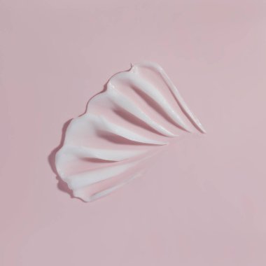 Pembe arka planda beyaz güzellik kremi lekesi. Kozmetik cilt ürünü dokusu. Yüz kremi, vücut losyonu sürgüsü.