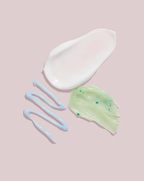 Composition of various cosmetic mask, cream or exfoliant smear on a pink background. Beauty texture. Sample of a cosmetic product.