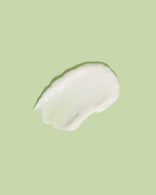 Beauty cream smear smudge on green background. Cosmetic skincare product texture. Face cream, body lotion swipe swatch 