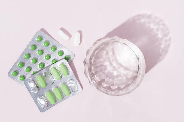 ピンクの背景にブリスター カプセル 水のガラスの中の丸薬 ビタミン 健康複合体の治療のための準備 — ストック写真