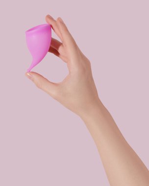 Pembe arka planda tekrar kullanılabilir regl fincanı olan bir kadın el.
