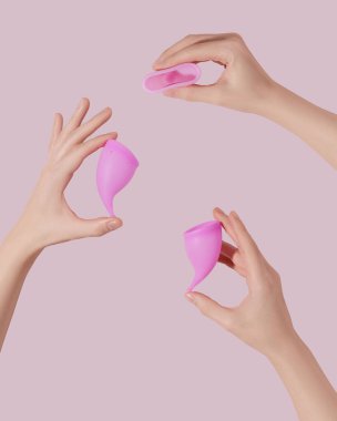 Pembe arka planda tekrar kullanılabilir regl bardakları olan kadın elleri