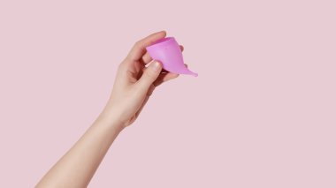 Pembe arka planda tekrar kullanılabilir regl fincanı olan bir kadın el.