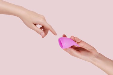 Pembe arka planda tekrar kullanılabilir regl fincanı olan bir kadın el.
