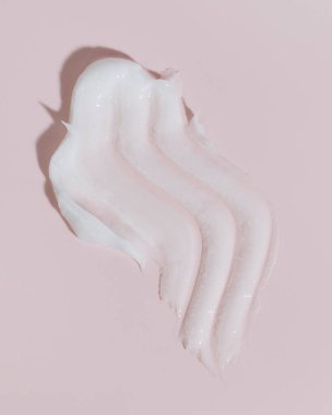 Pembe arka planda beyaz güzellik kremi lekesi. Kozmetik cilt ürünü dokusu. Yüz kremi, vücut losyonu sürgüsü. 