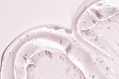 Pembe arka planda şeffaf sıvı jel. Kozmetik cilt ürünü dokusu. Yüz kremi, vücut losyonu sürgüsü.