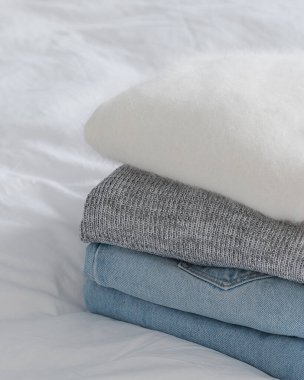 Beyaz bir yatağın üzerinde açık mavi kot pantolon ile düzgünce katlanmış rahat giysiler. Organizasyon gardırobu - boş kopya alanı.