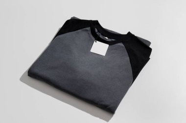 Katlanmış siyah ve gri gömlekli, boş giyim etiketli, hafif arkaplanda markalaşma modeli