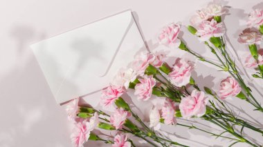 Beyaz zarf ve pembe karanfiller. Anneler Günü için ideal, düğün davetiyeleri, tebrik kartları, bahar kutlamaları, ya da minimalist kırtasiye markaları. 