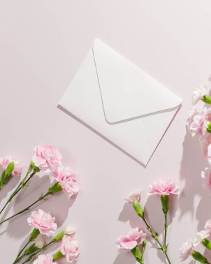 Beyaz zarf ve pembe karanfiller. Anneler Günü için ideal, düğün davetiyeleri, tebrik kartları, bahar kutlamaları, ya da minimalist kırtasiye markaları. 