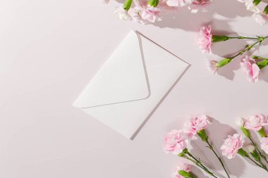 Beyaz zarf ve pembe karanfiller. Anneler Günü için ideal, düğün davetiyeleri, tebrik kartları, bahar kutlamaları, ya da minimalist kırtasiye markaları. 
