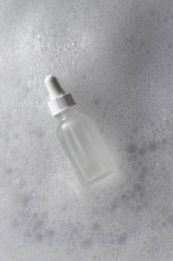 Temiz sabun köpüğünün içinde yüzen cam damlası şişesi. Kozmetik modelleme, cilt serumu reklamları ya da güzellik ürünü sunumu için mükemmel..