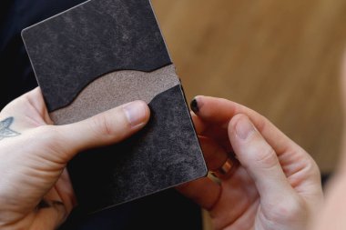 Leather wallet edge finishing during handcrafting process. Close-up of artisan hands applying black edge paint. 